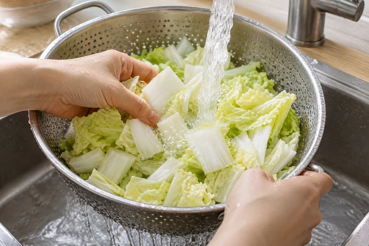 Chopped napa cabbage rinsing under cold running water in a stainless colander.
