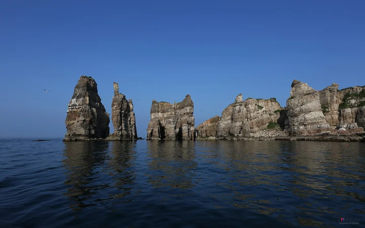Tall weathered sea cliffs reflected in calm blue water beside Baengnyeongdo.