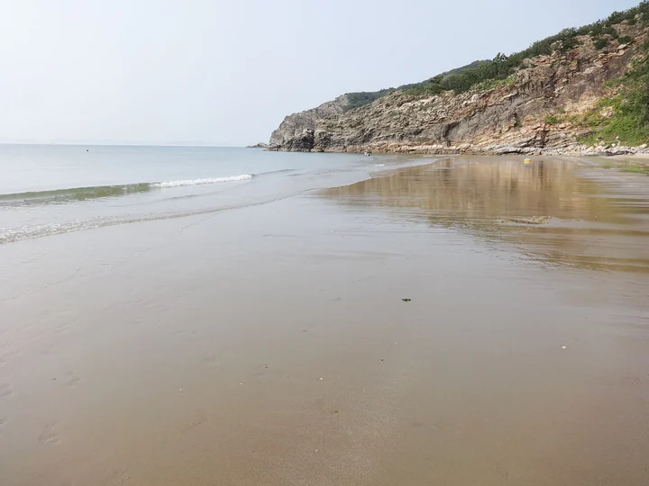 Wet sand and gentle surf below the rocky green headland at Jiduri Beach on Daecheongdo.