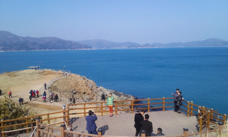 Blue sea and distant mountains beyond visitors on the viewing deck at Windy Hill, Geoje.