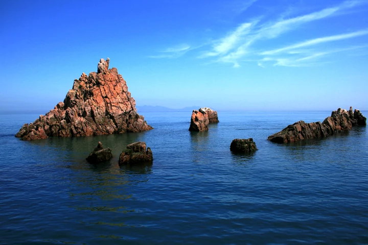 Jagged reddish rock formations rise from deep blue water off Hongdo.