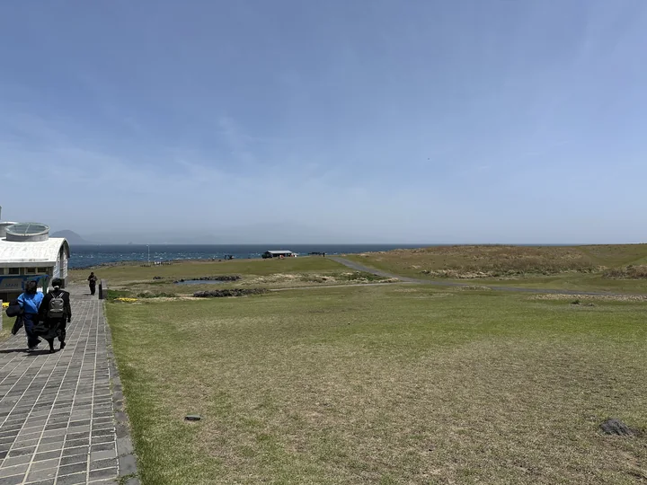 A paved walking path crosses Marado’s low grassland, with the blue sea along the horizon.