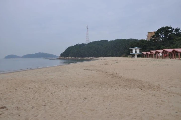 A quiet sandy beach and red shade shelters below the wooded shore of Seungbongdo.