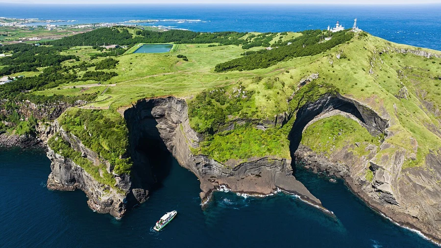 Green Udobong and its lighthouse rise above sculpted volcanic cliffs and deep blue water on Udo.