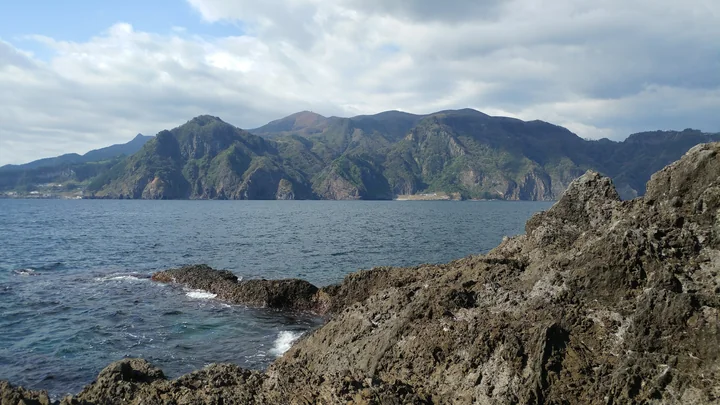 The steep green northeastern coastline of Ulleungdo rises above blue water, seen from nearby Jukdo.