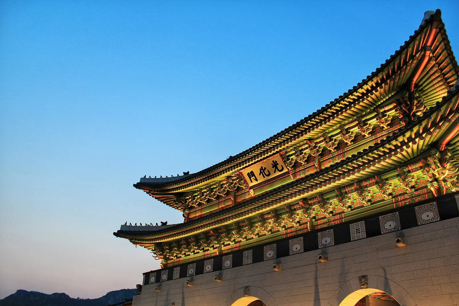 The illuminated painted eaves of Gwanghwamun against a clear evening sky.